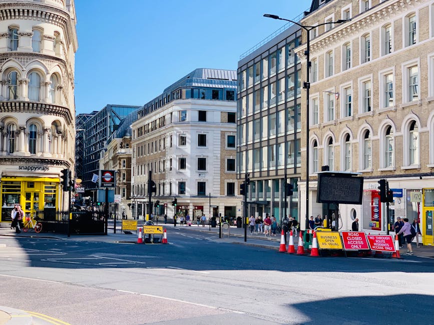 A city street scene in London featuring a variety of buildings with different architectural styles, including a historic cream-colored building with rounded bay windows and decorative detailing on the